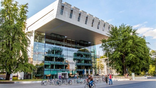 Das Foto zeigt ein modernes Gebäude mit Glasfassade und Fahrrädern im Vordergrund