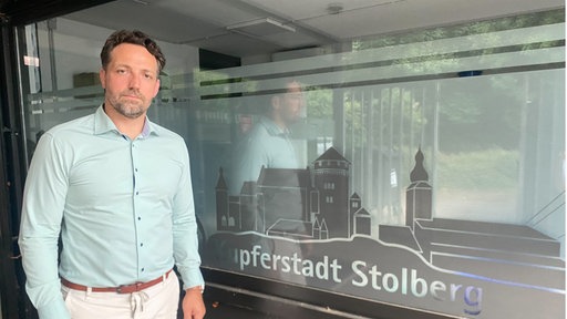 Stolbergs Bürgermeister Patrick Haas steht vor einem Fenster mit der Aufschrift "Kupferstadt Stolberg".