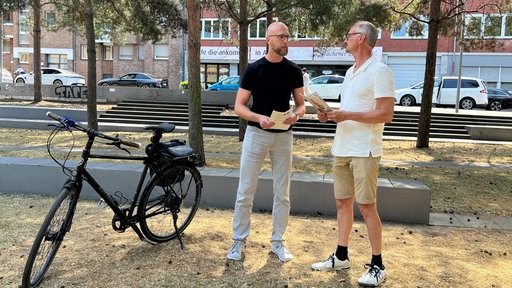 Patrick Hof vom ADFC und Ralf Oswald, Sprecher des Radentscheids, stehen neben einem Fahrrad auf einer Wiese. 