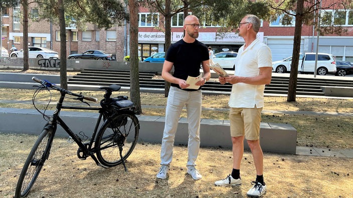 Patrick Hof vom ADFC und Ralf Oswald, Sprecher des Radentscheids, stehen neben einem Fahrrad auf einer Wiese. 
