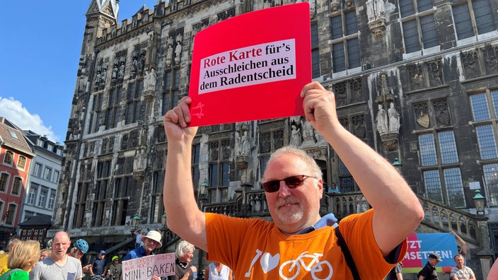 Ein Mann hält beim Protest ein Schild mit der Aufschrift "Rote Karte fürs Ausschleichen aus dem Radentscheid" hoch
