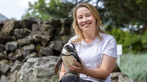 Janina Dötzer sitzt im Tierpark mit einem Pinguin auf dem Schoß als Jüngste Zoochefin Deutschlands und lacht in die Kamera