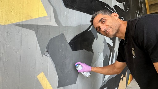 Alex Shifferaw mit Spraydose an der Graffiti-Wand unter der Brücke