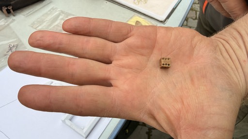 Auf einer Hand liegt ein kleiner Würfel.