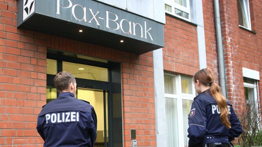 Zwei Polizisten stehen vor einer Fassade worauf 'Pax-Bank' geschrieben steht
