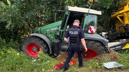 Traktor und Anhänger nach Unfall im Straßengraben. Ein Polizist geht darauf zu.