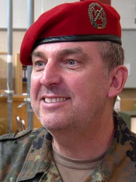 Ein Mann mit roter Soldaten-Mütze schaut lächelnd an der Kamera vorbei