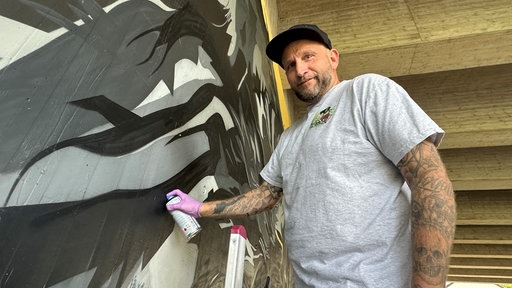 Chris Hoven mit Spraydose an seiner Graffiti-Wand unter der Brücke