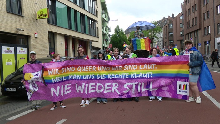 Mehrere Demonstranten, teils mit Regenbogenflaggen, tragen ein Plakat
