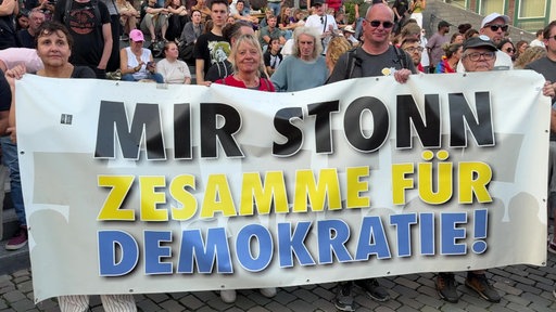 Teilnehmende einer Demonstration am Katschhof in Aachen halten einen Banner mit der Aufschrift: "Mir stonn zesamme für Demokratie!"