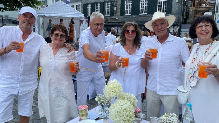 Eine Gruppe von Menschen, alle in weiß gekleidet, mit einem Aperol in der Hand.