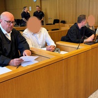 Gerichtssaal, die Angeklagten und ihre Anwälte, daneben die Dolmetscherin des einen Angeklagten