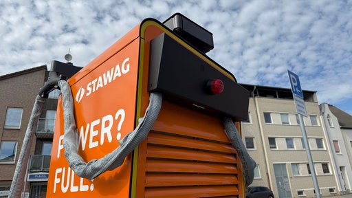 Eine orangefarbene Ladesäule für Elektroautos, an der die Kabel ummantelt sind und eine rote Alarmleuchte angebracht ist