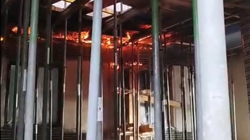 Flammen an der Decke eines Raumes, in dem zahlreiche Stahlstützen stehen.