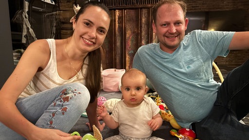 Eine junges Paar mit einem sditzenden Baby auf einer Spieledecke