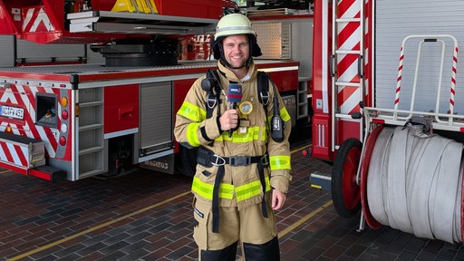 WDR-Reporter Florian Bechholz in Feuerwehrmontur in der Fahrzeughalle.