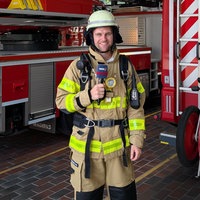 WDR-Reporter Florian Bechholz in Feuerwehrmontur in der Fahrzeughalle.