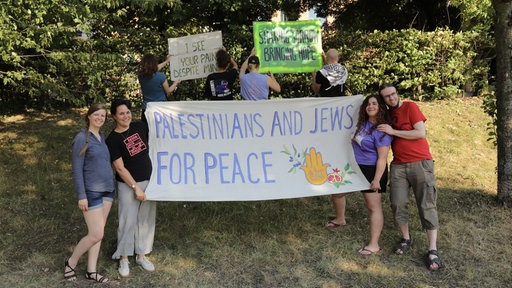 Eine Gruppe hält mehrere Schilder hoch, verteilt um einen Banner, auf dem Palestinians and Jews for Peace steht