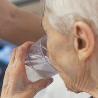 Eine ältere Frau mit kurzen weißen Haaren, trinkt aus einem Glas Wasser.