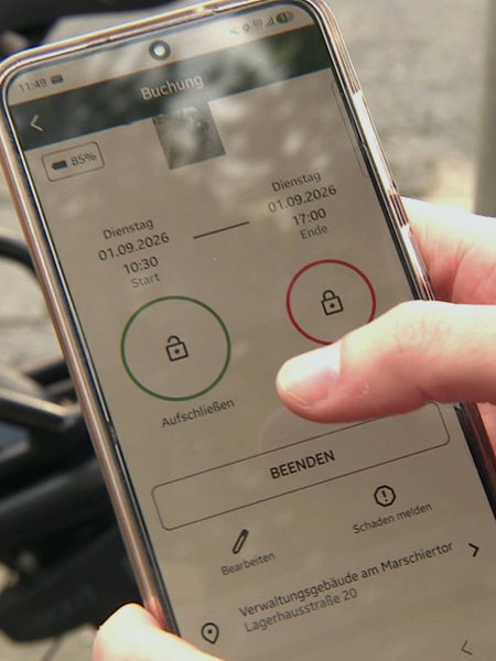 Eine Hand hält ein Handy, das eine App zur Lastenrad-Ausleihe geöffnet hat.