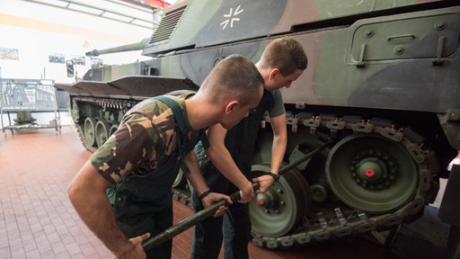 Zwei Männer in Bundeswehr-Kleidung schrauben an einem Panzer in einer Werkstatt