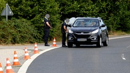 Zwei Polizisten kontrollieren an einer Straße einen SUV mit zwei Personen