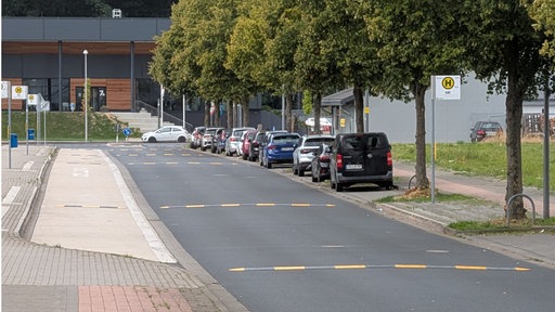 Eine Straße an einer Bushaltestelle. Auf der Straße befinden sich schwarz-gelbe Fahrbahnschwellen.