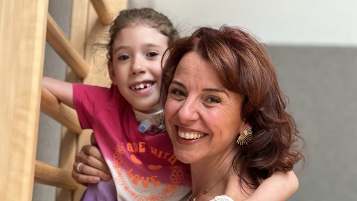 Eine Frau die ein Kind in den Armen hält, das Kind hält sich an einem Gerüst fest, beide lächeln