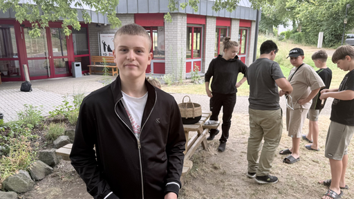 Pavlo steht neben den anderen Kindern vor einem Gebäude und schmunzelt leicht.