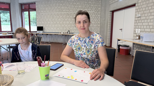 Nataliia Lompei sitzt neben einem Kind am Tisch. Vor ihnen liegen bunte Zeichnungen.