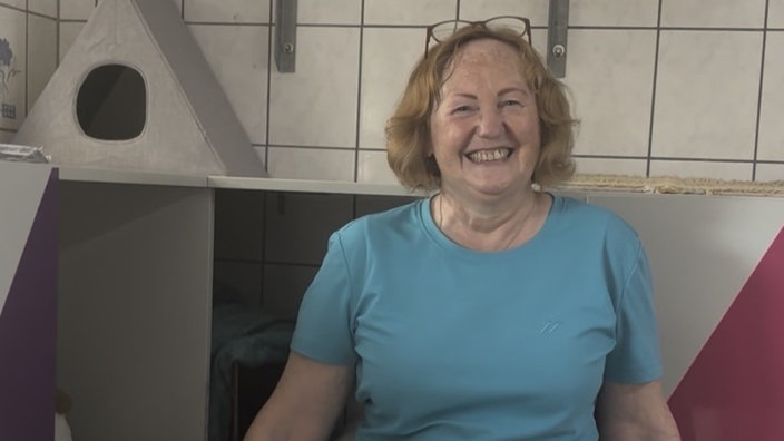 Eine Frau steht vor einer Wand mit Katzenbäumen und Regalen