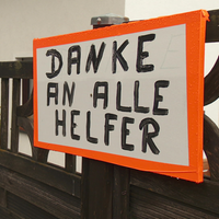 Ein Gartenzaun an dem Zwei Schilder angebracht sind. Darauf steht "Danke an alle Helfer".