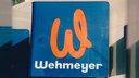Ein Schild von der Firma Wehmeyer, mit orangem 'W' auf blauem Hintergrund