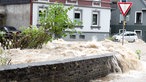Auf einer überfluteten Straße schießt das Wasser über eine Mauer