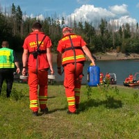 Drei Personen laufen auf Wasser zu.Einer von ihnen trägt eine gel- grüne Warnweste, die anderen beiden sind in Rettungsausrüstung der DLRG