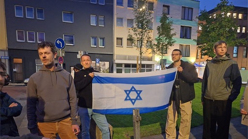 Mehrere Menschen versammeln sich vor einer Fahne Israels