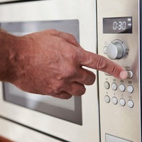 eine Hand drückt den Start-Knopf einer Mikrowelle, eingestellt ist eine Zeit von 30 Sekunden