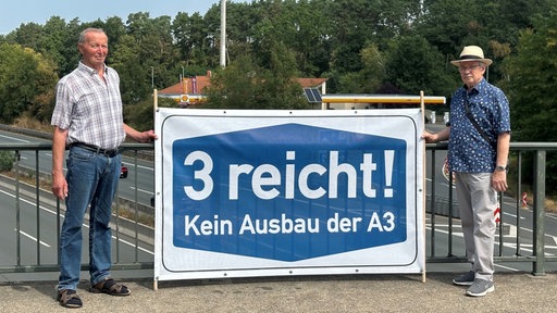 Zwei Männer halten ein Banner mit der Aufschrift "3 reicht! Kein Ausbau der A3"