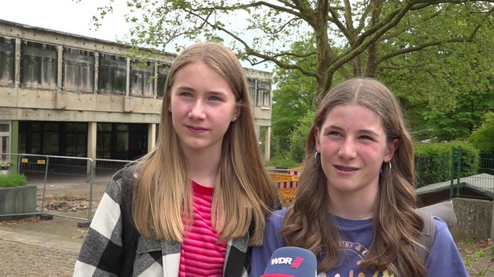 Zwei Mädchen mit langen Haaren vor einem abgebrannten Schulgebäude