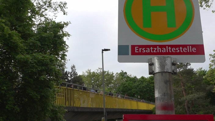 Ein Schild Ersatzhaltestelle und Schüler, die im Hintergrund über eine Brücke laufen