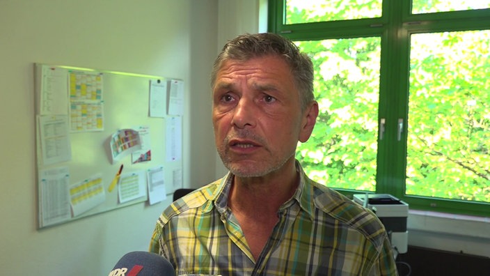 Ein mittelalter Mann mit angegrauten Haaren in einem Büro vor seinem Schreibtisch