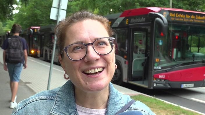 Eine lachende Mutter mit runder Brille vor einem Schulbus