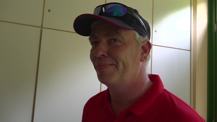 Ein älterer Mann mit rotem Polo-Shirt, dunkler Kappe und Sonnenbrille oben drauf