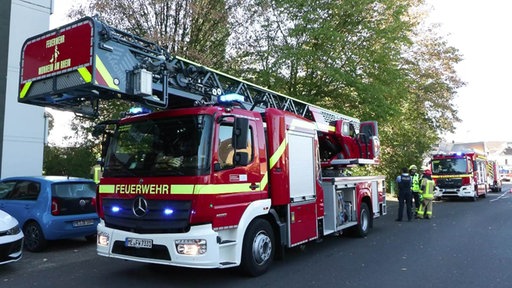 Zwei Feuerwehrautos stehen vor einem Haus, daneben einige Feuerwehrleute