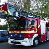 Zwei Feuerwehrautos stehen vor einem Haus, daneben einige Feuerwehrleute