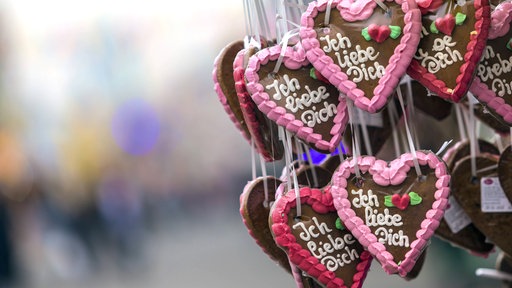 Lebkuchenherzen hängen an einem Stand auf einer Kirmes. darauf steht: Ich liebe Dich