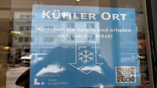 ein einlaminiertes Schild ist an einer Scheibe befestigt, darauf steht "Kühler Ort - Kommen Sie herein und erholen Sie sich von der Hitze!"