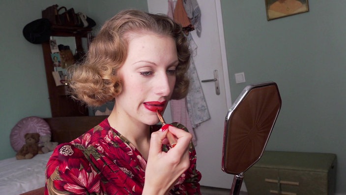 Lenina trägt sich mit einem Lippenstift rote Farbe auf die Lippen