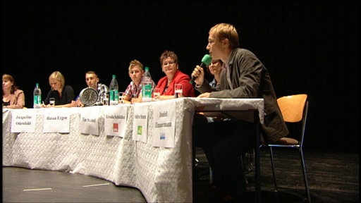 Vorne ist Daniel Zimmermann von der Peto zu sehen, im Hintergrund sitzen an einem langen Tisch Vertreter weiterer Parteien.