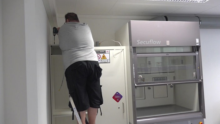 Ein Arbeiter steht auf einer Leiter und hantiert mit einer Bohrmaschine auf einem Schrank